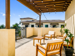 Communal outdoor balcony area featuring cushioned wood furniture at Gladstone Senior Villas.